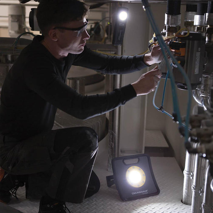 Técnico con gafas de seguridad trabajando en tuberías industriales con luz LED portátil de alta potencia