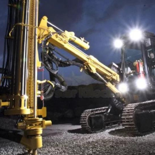 Maquinaria pesada Caterpillar con faros LED encendidos operando en obra nocturna sobre terreno de grava