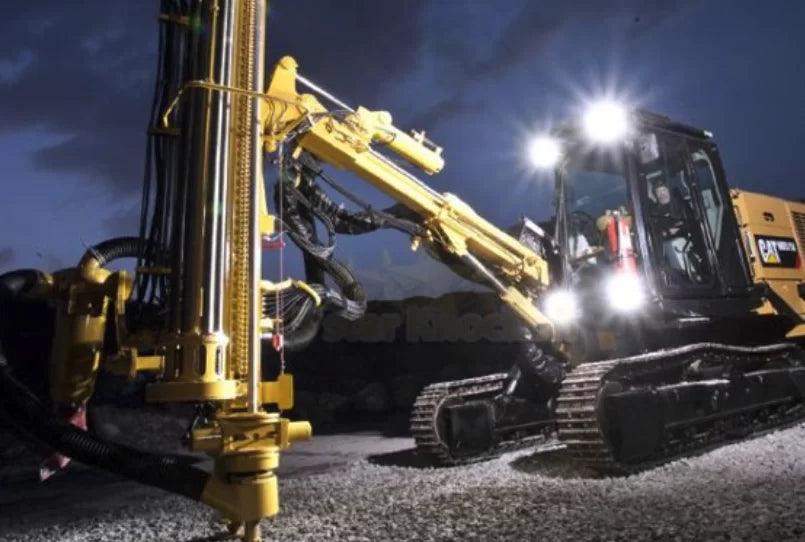 Maquinaria pesada Caterpillar con faros LED encendidos operando en obra nocturna sobre terreno de grava