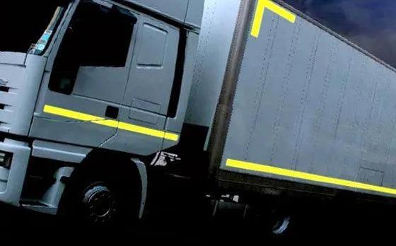 Camión gris con cinta reflectante amarilla 3M en la cabina y caja lateral en ambiente oscuro