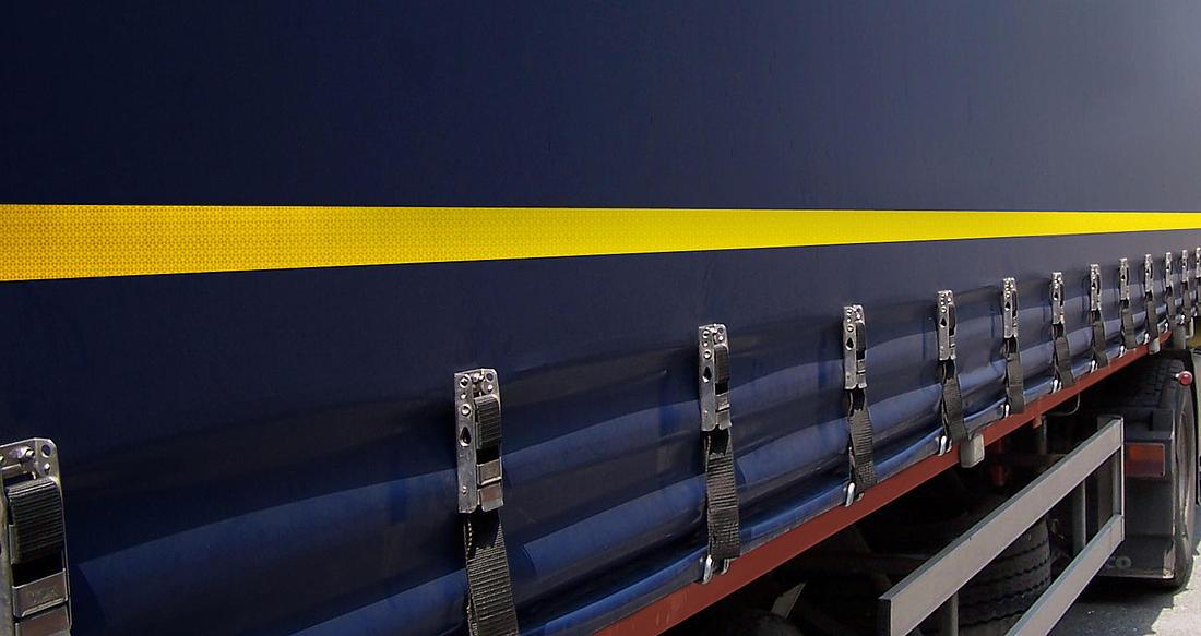 Cinta reflectante amarilla instalada en la lona lateral de un camión azul para seguridad vial