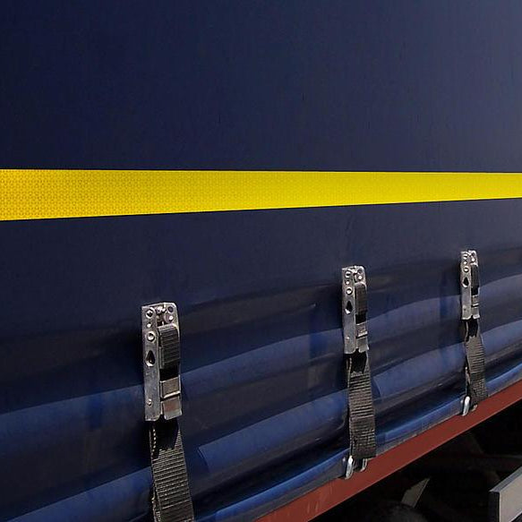 Cinta reflectante amarilla instalada en la lona lateral de un camión azul para seguridad vial