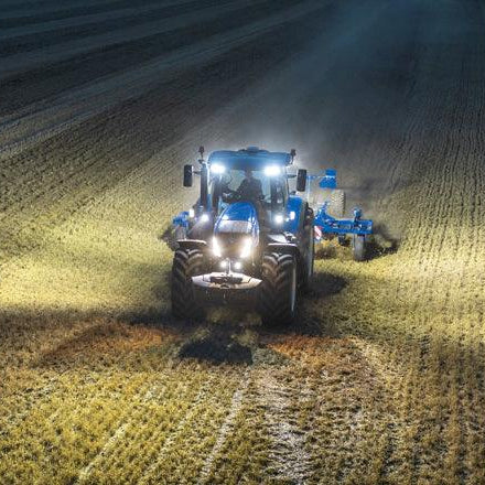 Tractor agrícola azul con luces LED trabajando de noche en un campo sembrado