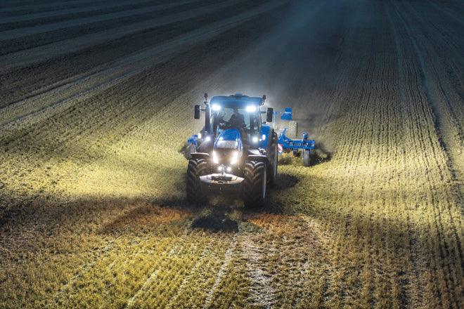 Tractor agrícola azul con luces LED trabajando de noche en un campo sembrado