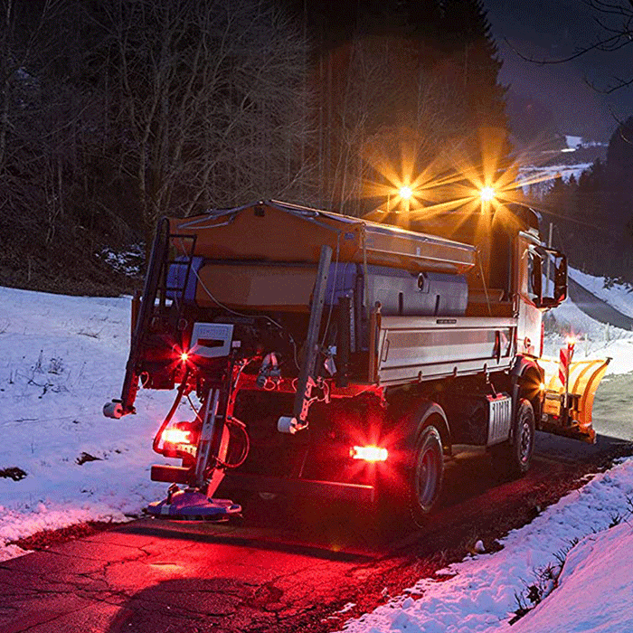 Camión quitanieves con luces LED encendidas limpiando carretera nevada de noche